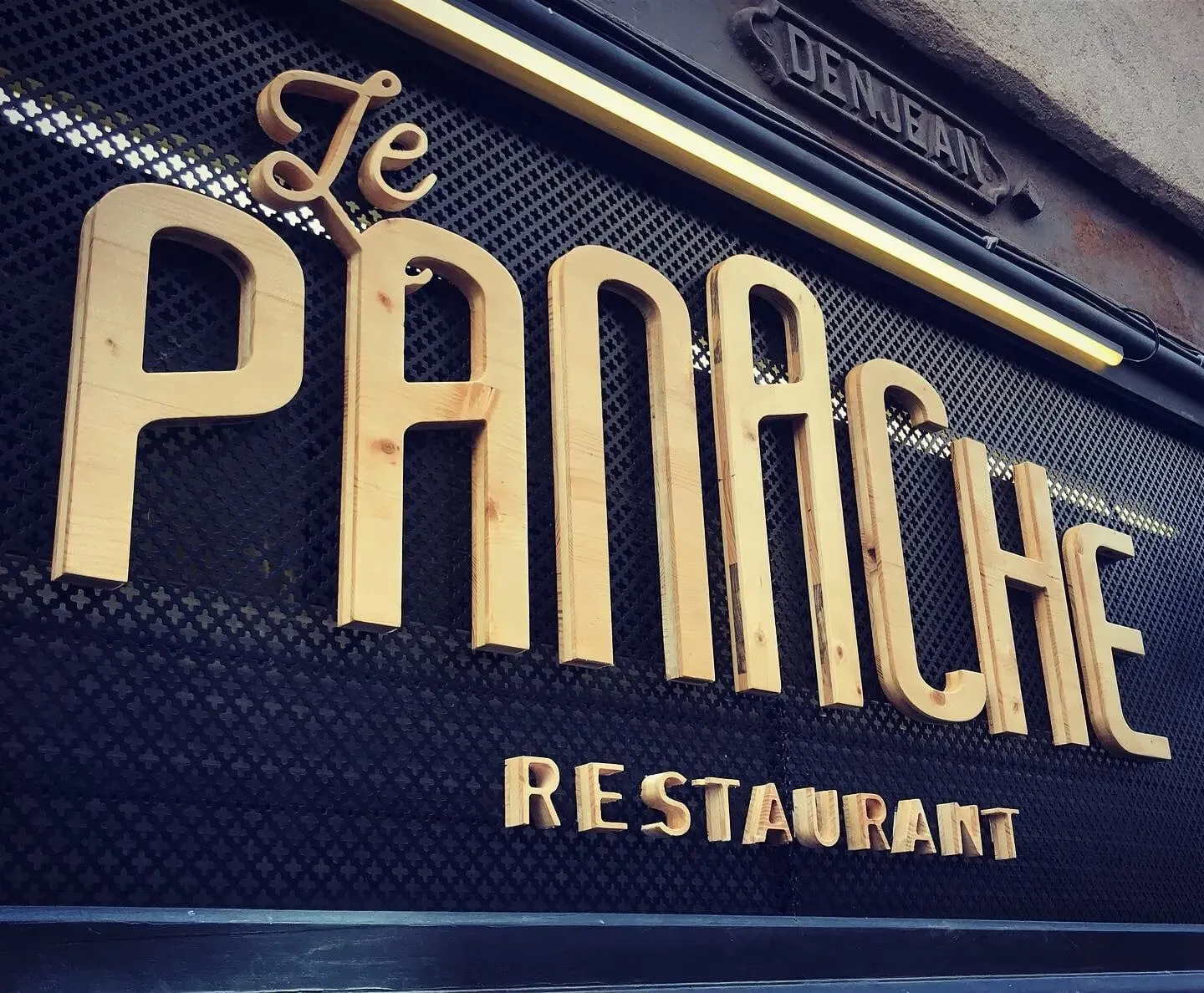 Enseigne en lettres lumineuses du restaurant Le Panache sur façade sombre