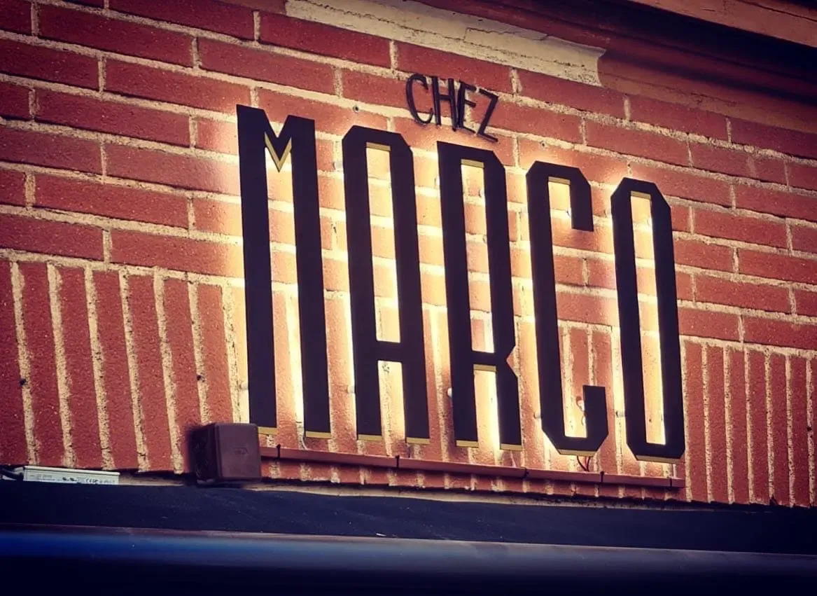 Lettres rétroéclairées Chez Marco sur un mur de briques